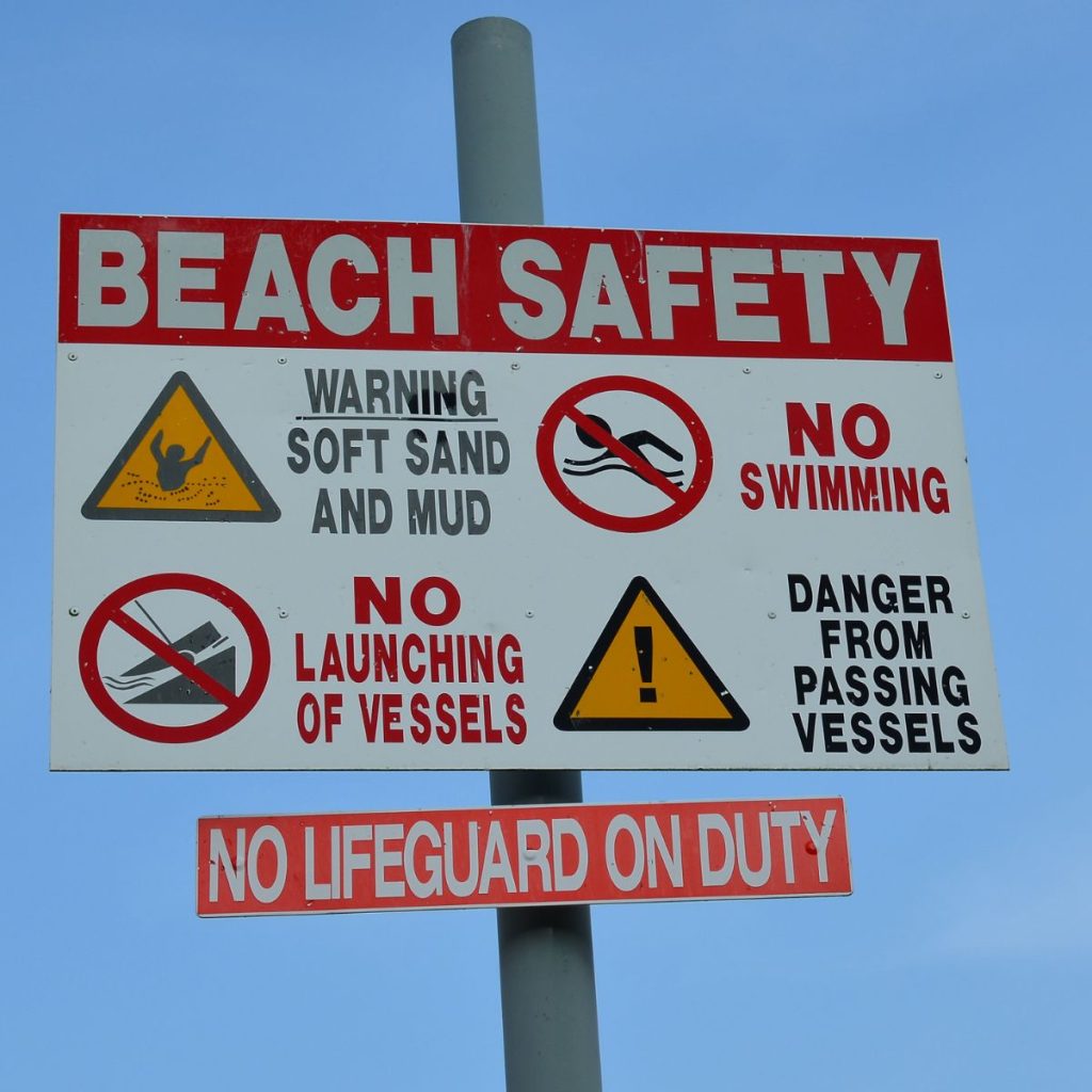 Beach safety sign with multiple warnings.