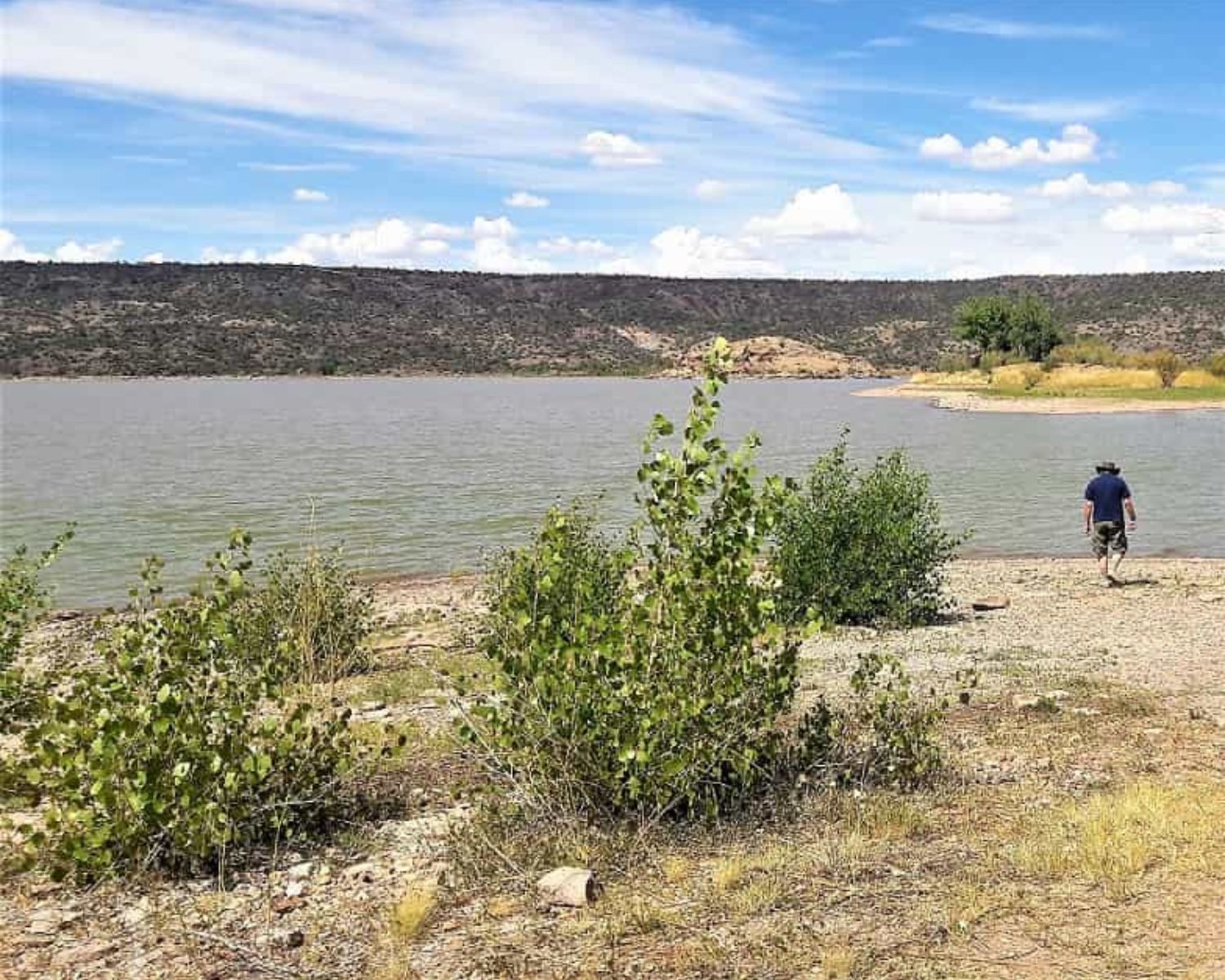 man walking to shore of a desert lake.