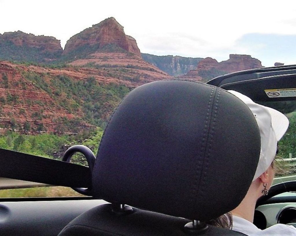 A woman driving a convertible along scenic red rock cliffs.