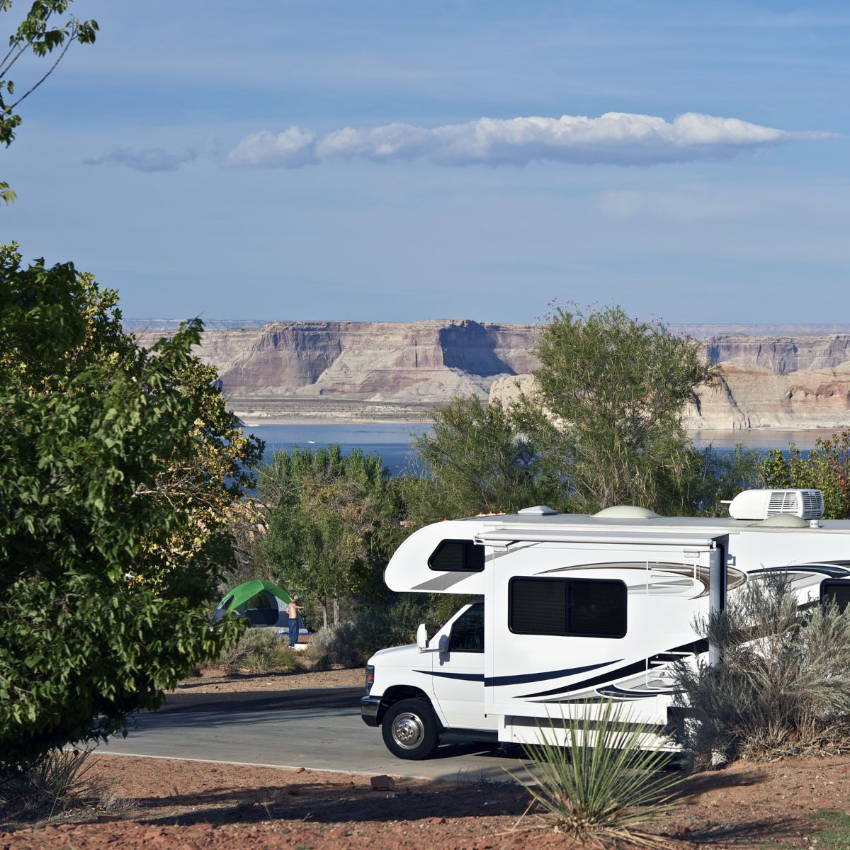 Rv parked by the lake and a green tent in the distance.